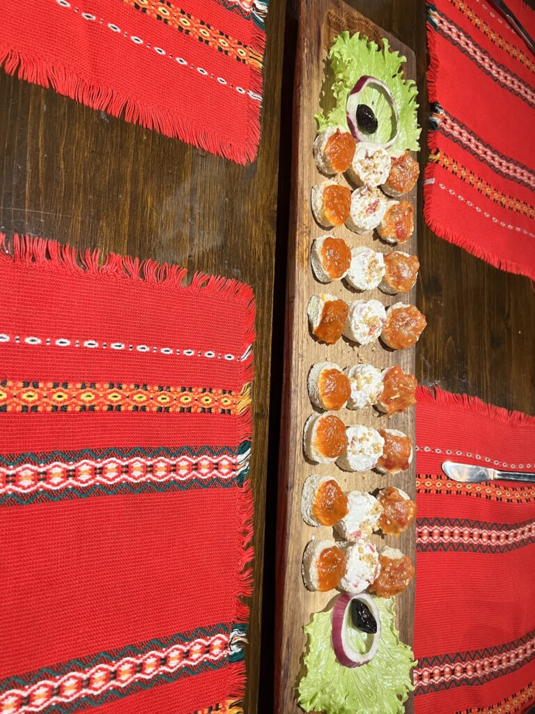 Close-up of traditional Bulgarian food on a rustic wooden table, featuring a vibrant Shopska salad with tomatoes, cucumbers, and feta cheese, alongside a hearty plate of Banitsa pastry and grilled kebapche. A bowl of tangy tarator soup sits nearby, garnished with fresh dill, capturing the authentic flavors of Bulgaria. Perfect for food lovers exploring Balkan cuisine; where to eat in Sofia